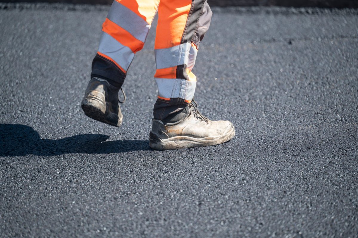 Bauarbeiter läuft auf neuem Asphalt, zu sehen ist der Bereich Knie bis Arbeitsschuhe