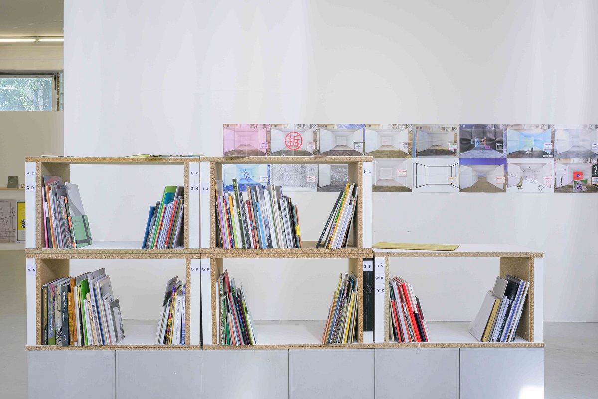 Ausstellungsansicht von "Abschied vom L6". Zu sehen sind Regalkubenm, die aus einem Teil der Ausstellungswand gebaut wurden. Darin befinden sich erste Kataloge von Freiburger Künstler_innen. Im Hintergrund sind Plakate der "GarageL6-Ausstellungen" zu sehen.