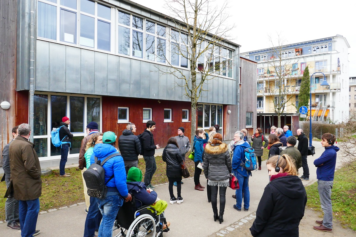 Gruppe mit Kopfhörern läuft oder fährt im Rollstuhl durch Wohnviertel