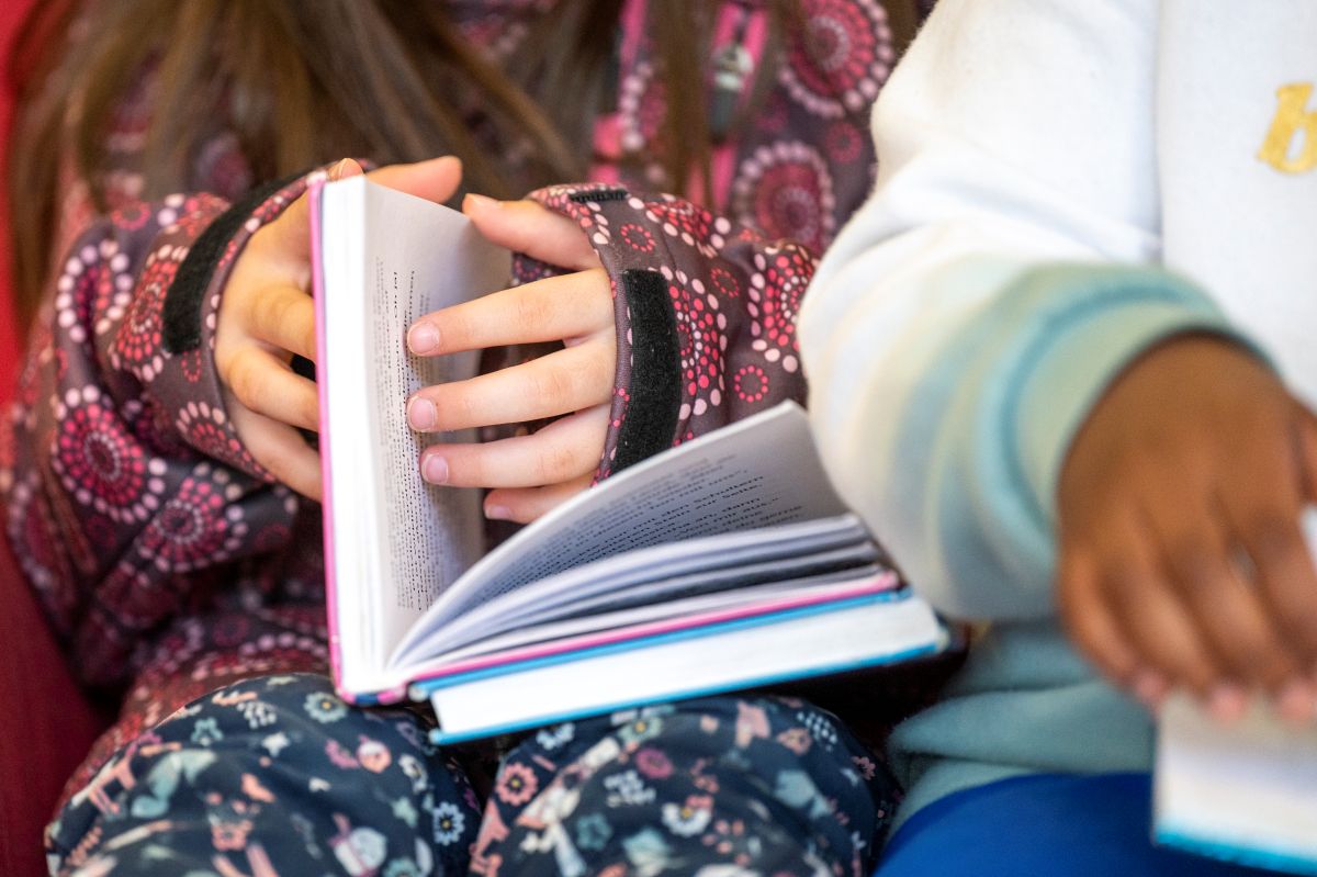 Zwei Paar Kinderhände blättern durch ein Buch