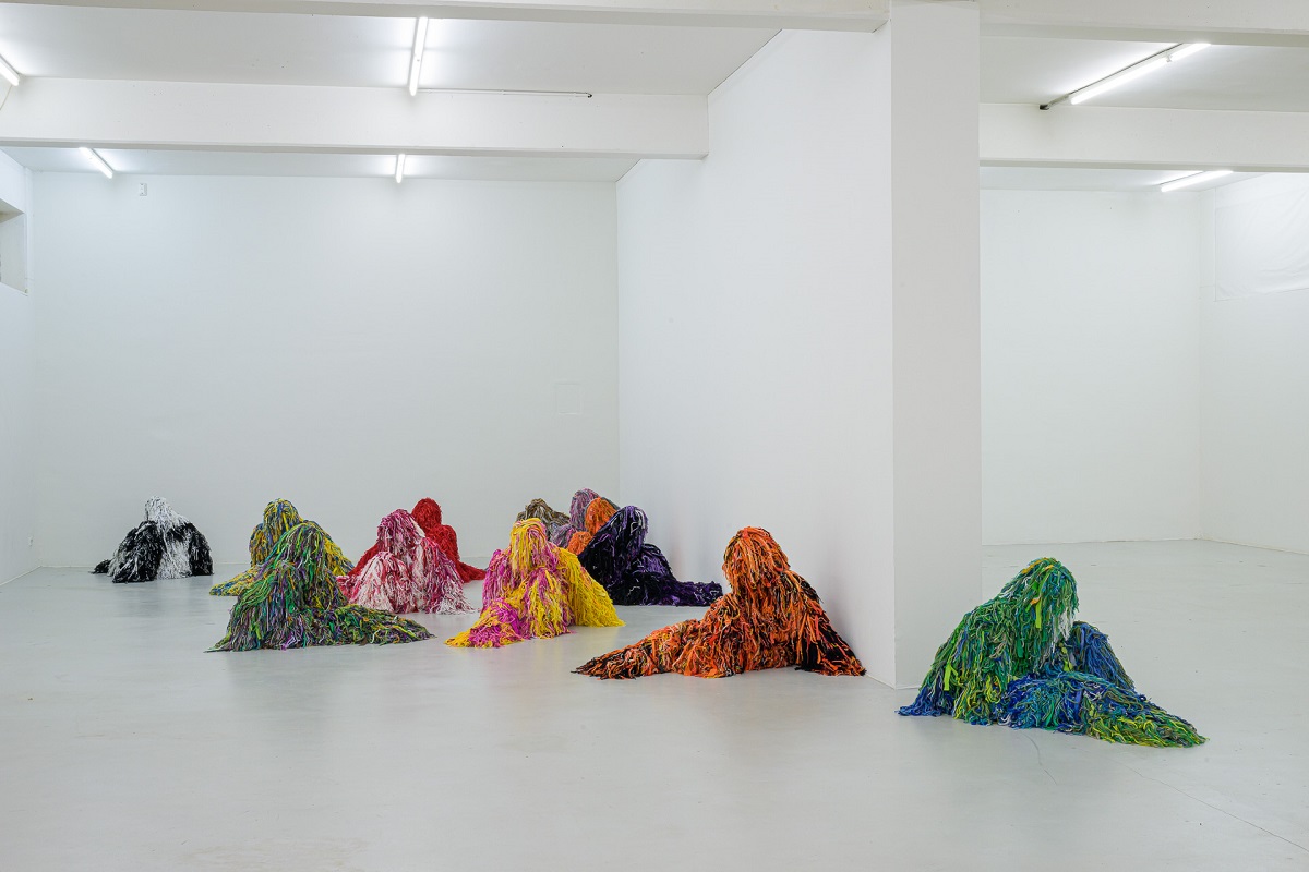 Ausstellungsansicht mit kauernden Figuren in bunten Tarnanzügen von Yongkuk Ko
