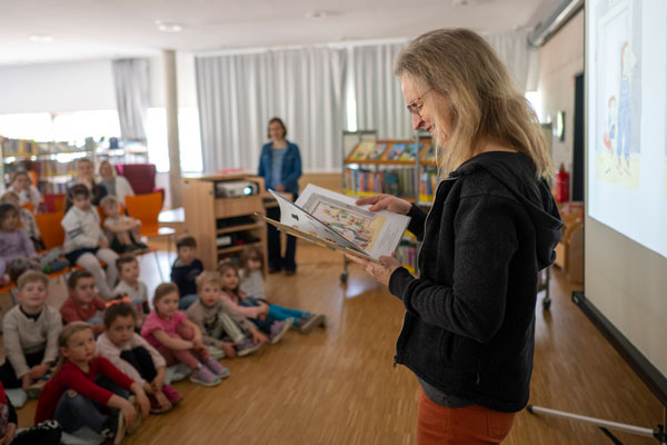 Eine Frau liest aus einem Buch vor, daneben eine Leinwand mit Schattenspiel