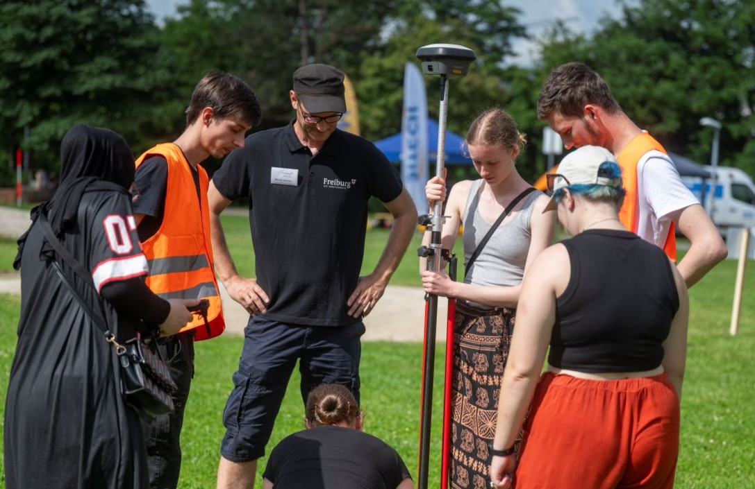 Eine Gruppe steht auf einer Wiese um ein Messgerät herum. 