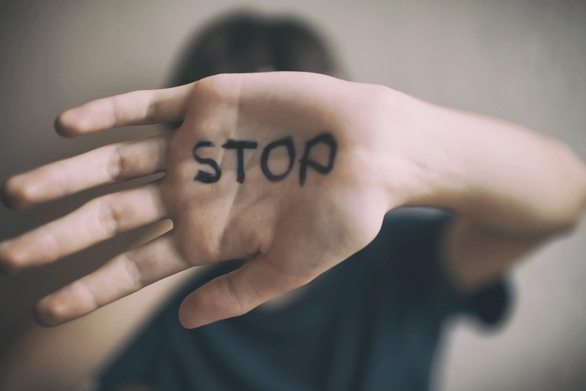 Mensch hält Hand vor das Gesicht mit Schriftzug "Stop"