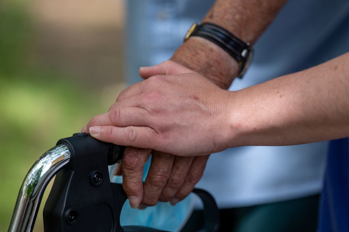 Eine Hand auf einer anderen Hand, die einen Rollator-Griff hält.