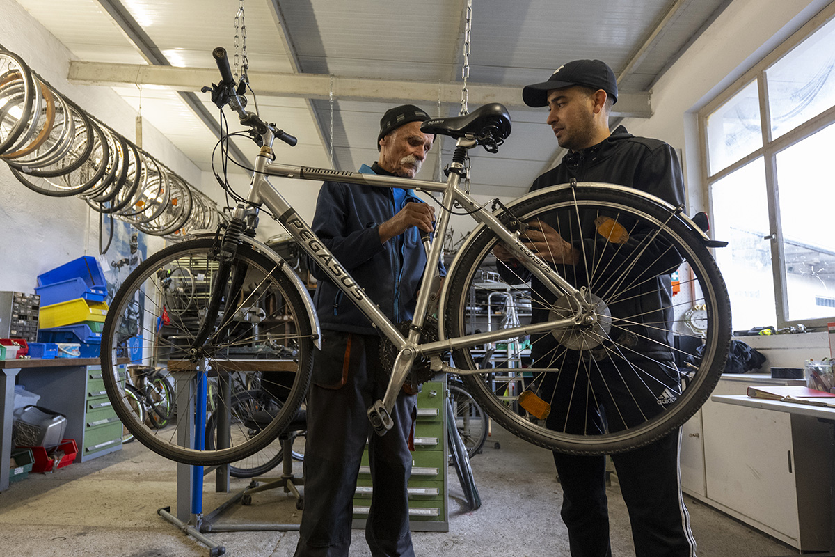 Zwei Personen stehen hinter einem Fahrrad und reparieren es