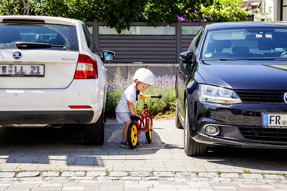 Kleines Kind parkt sein Laufrad zwischen zwei parkenden Autos