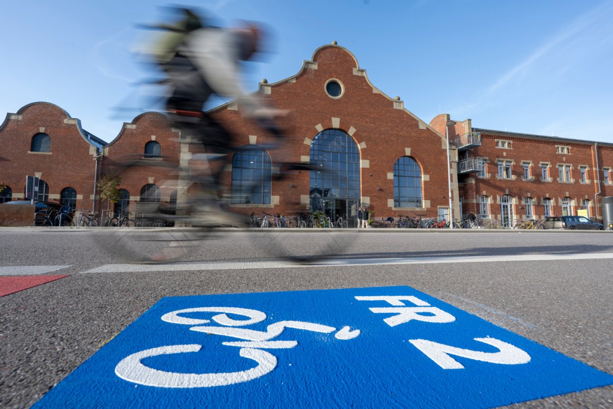 Im Vordergrund eine Straßenmarkierung für den FR2, dahinter fährt jemand Fahrrad. Im Hintergrund die Lokhalle des Güterbahnhofs Nord.