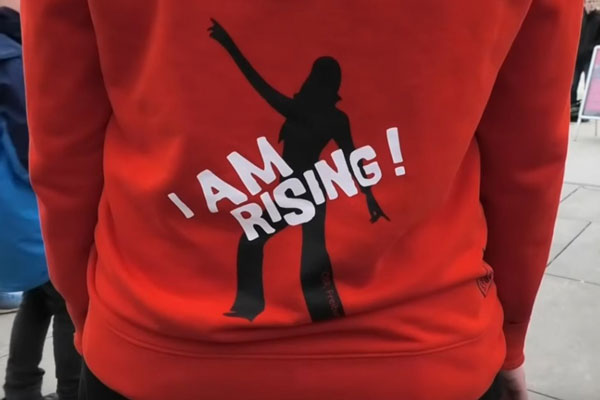 Person trägt roten Pulli mit Aufschrift "I am Rising"