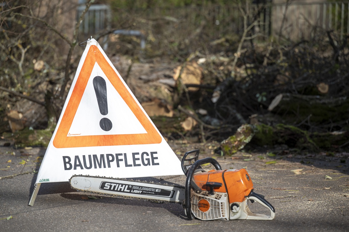 Ein Warndreieck "Baumpflege" auf dem Boden, davor eine Motorsäge.