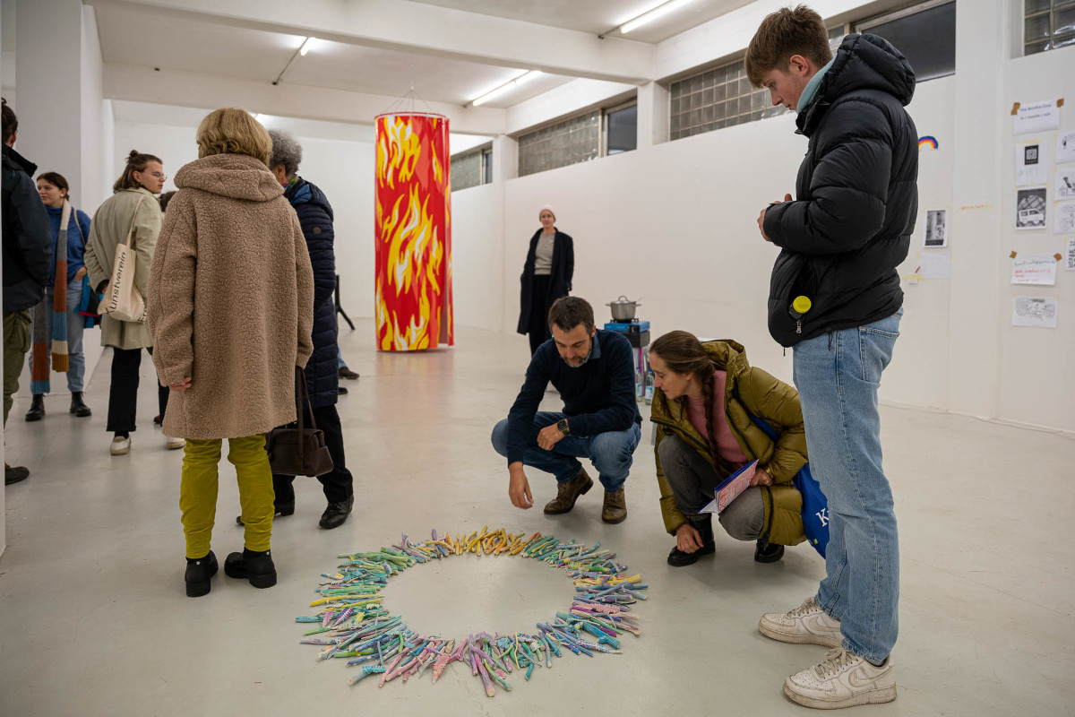 Ausstellungsansicht, Menschen im Gespräch, Kunstwerke von Hélène Bleys, Säule alsloderndes Feuer und Kreis aus bemalten Keramik-Kleinteiledie neu geordnet werden können
