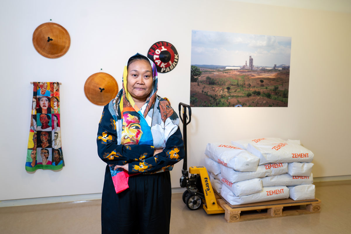 Eine Frau steht in traditionellem Gewand in einem Ausstellungsraum, im Hintergrund Exponate