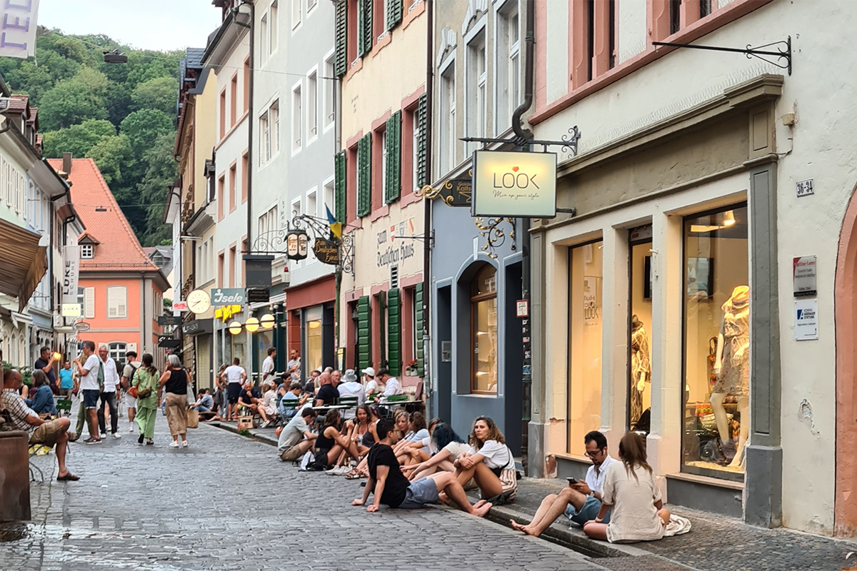 Menschen genießen die Kühle vom Bächle in dre Schusterstraße Menschen sitzen im Bächle in der Schusterstraße