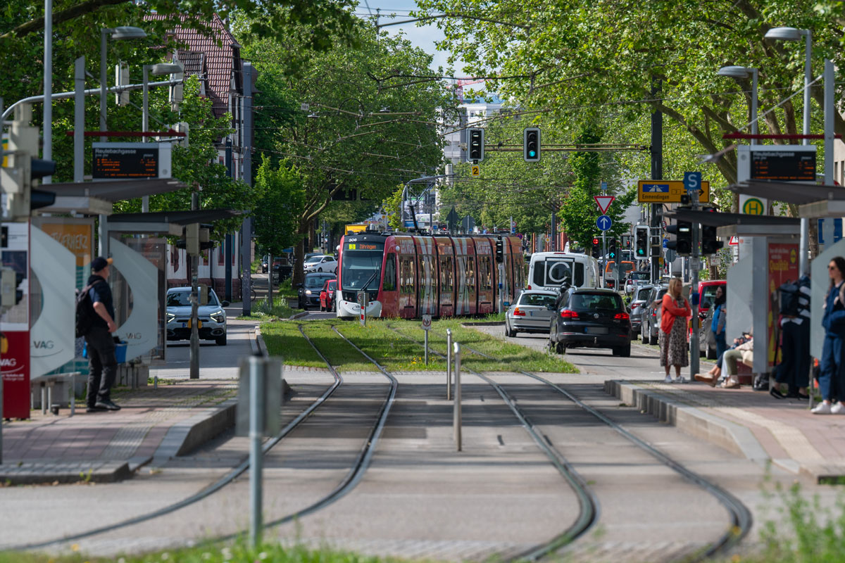 Straßenbahn fährt an Haltestelle ein, rechts und links Straße mit Menschen