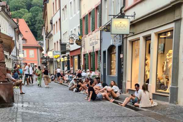 Auf einer belebten Ladenstraße sitzen Menschen vergnügt am Bächle