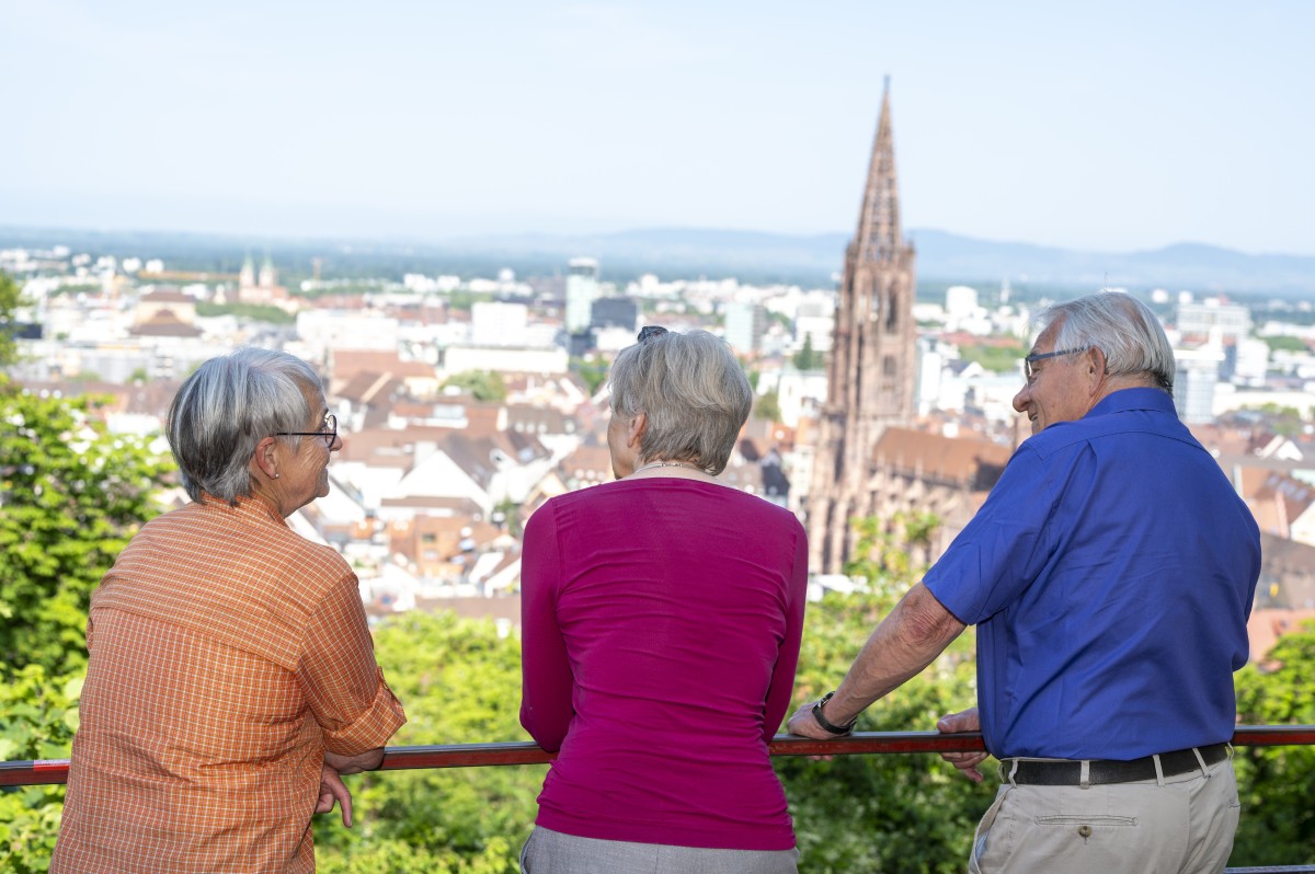Drei ältere Personen blicken auf Freiburg mit dem Münster. 