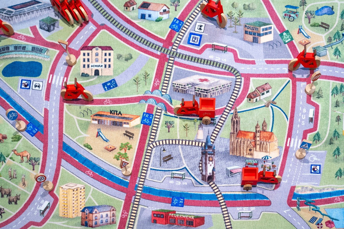 Freiburger Spielteppich, bedruckt mit Stadion, Münster und anderen Gebäuden, darauf kleine Spielzeugfahrzeugen