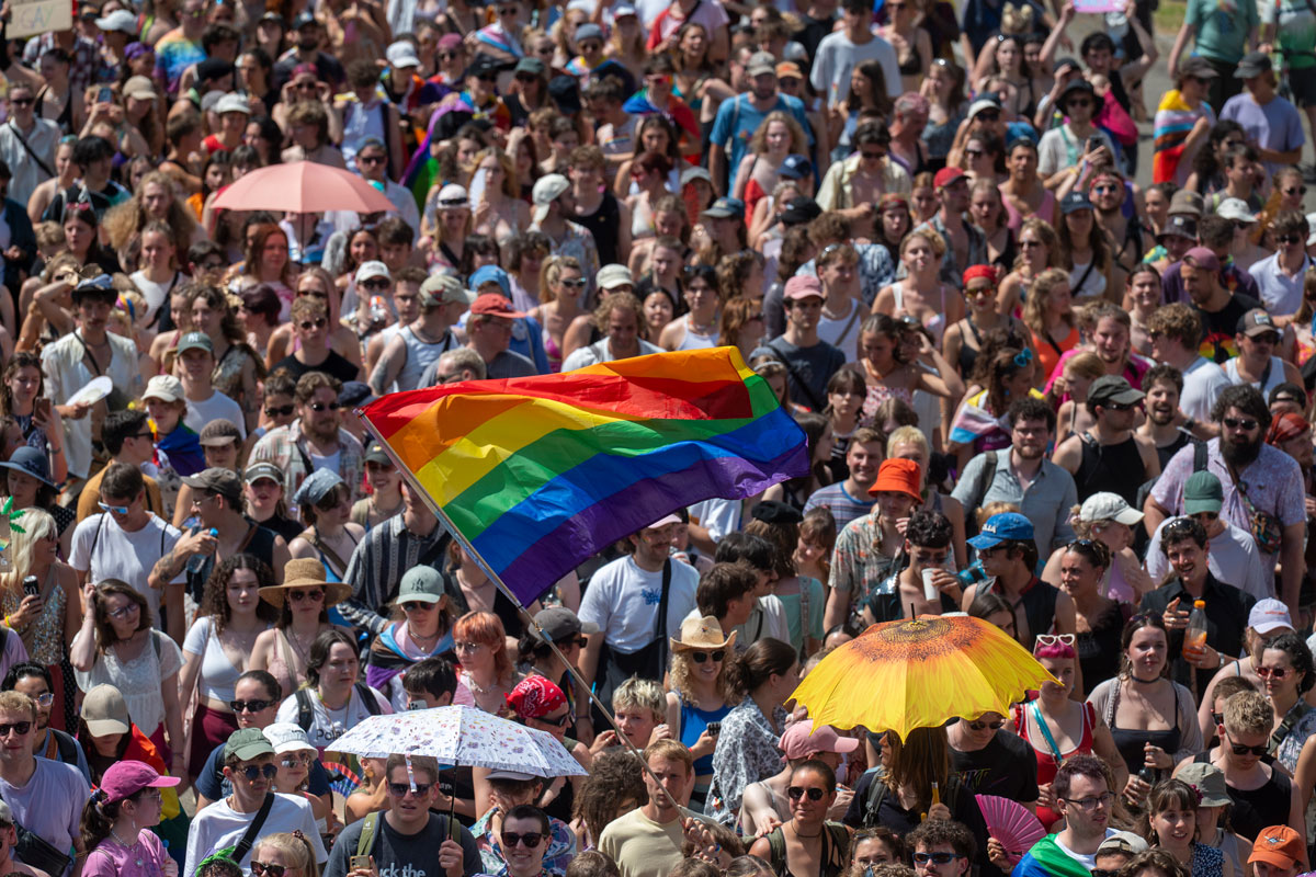 Viele Menschen im Hintergrund, im Vordergrund große Regenbogenfahne
