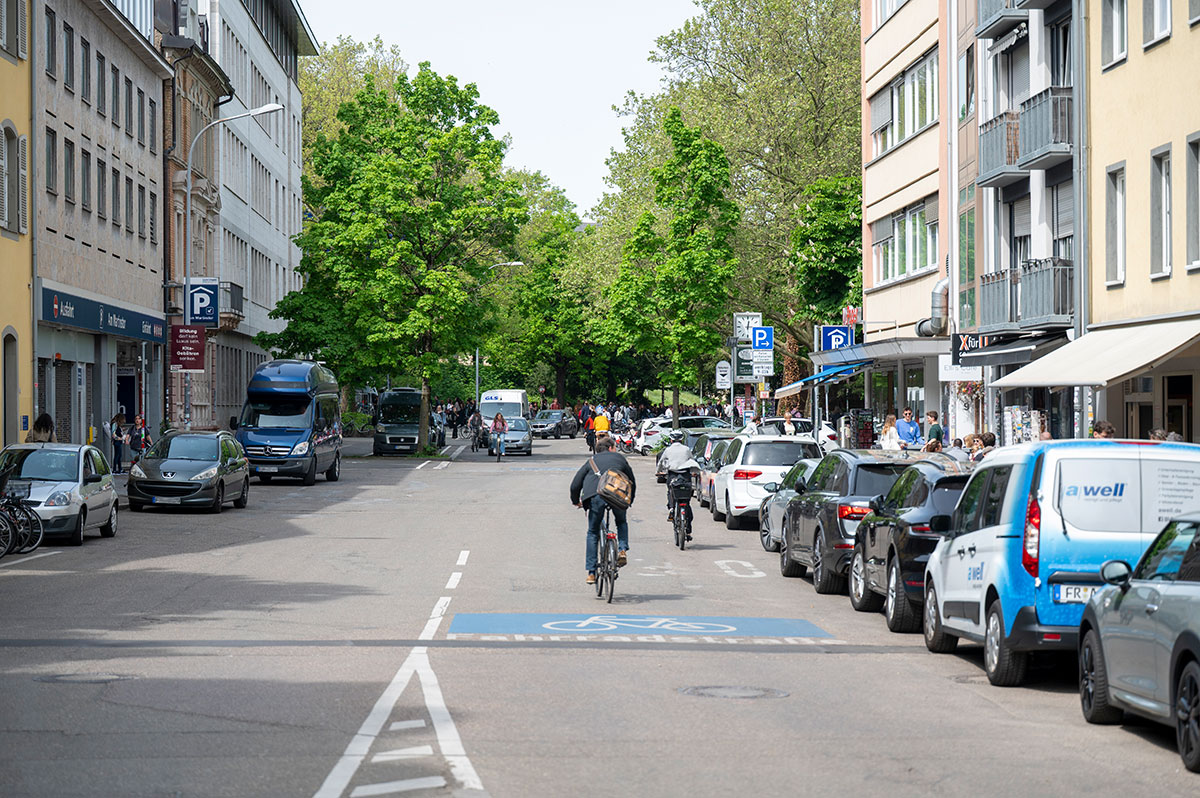 Zwei Fahrradfahrer fahren auf der Rempartstraße an parkenden Autos vorbei.