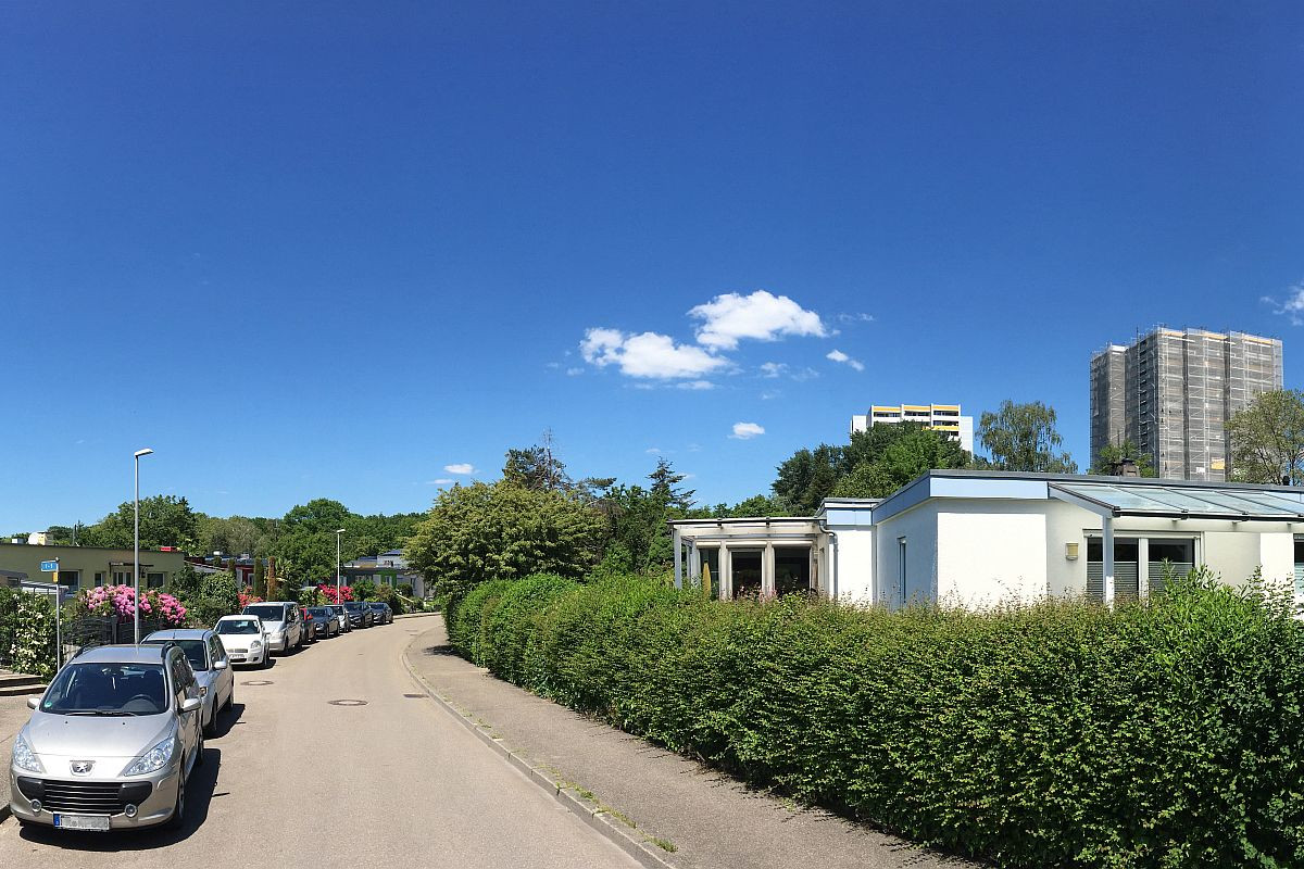 Straße mit parkenden Autos und niedrigen Häusern hinter Hecke